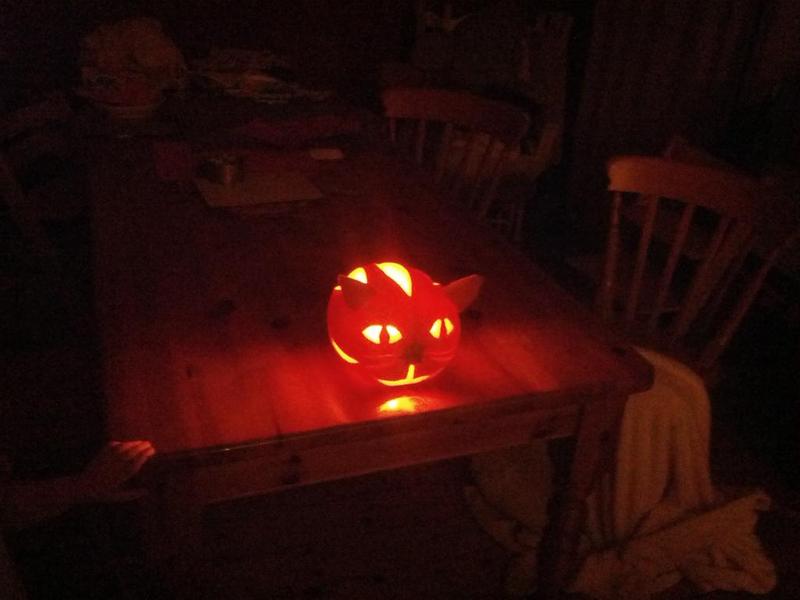 A pumpkin carved as a cat's face, sitting lit from within on our table.