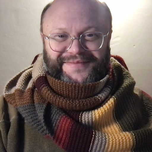 A photograph of Cian smiling at the camera, wearing a Doctor Who scarf.